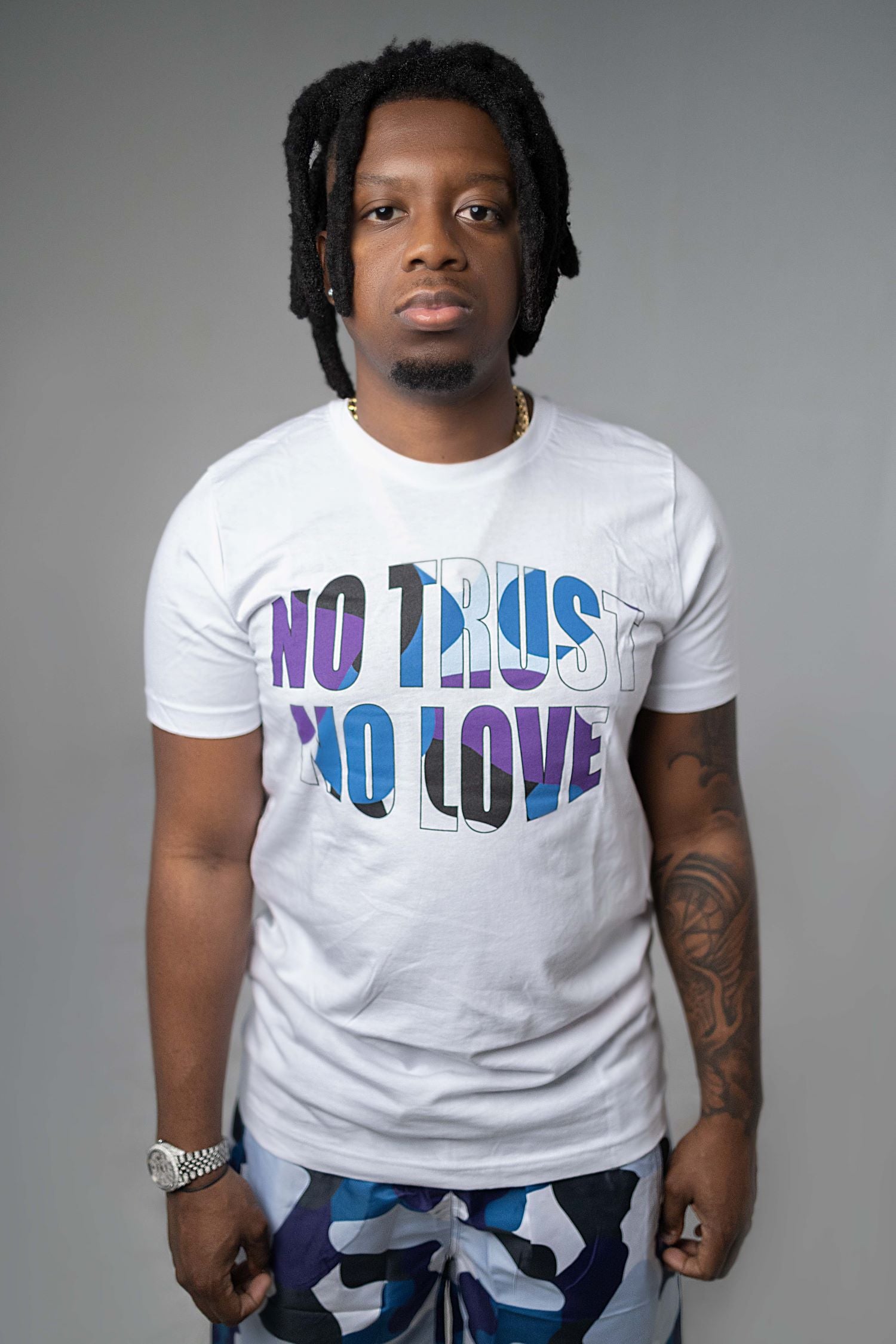 WHITE TSHIRT WITH LARGE BLUE CAMO ROUNDED "NO TRUST NO LOVE" PRINT ACROSS AT FRONT.